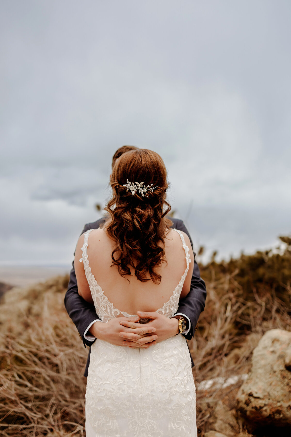 View of bride's back while being hugged by her new husband during their first look on top of a mountain in Boulder, Colorado