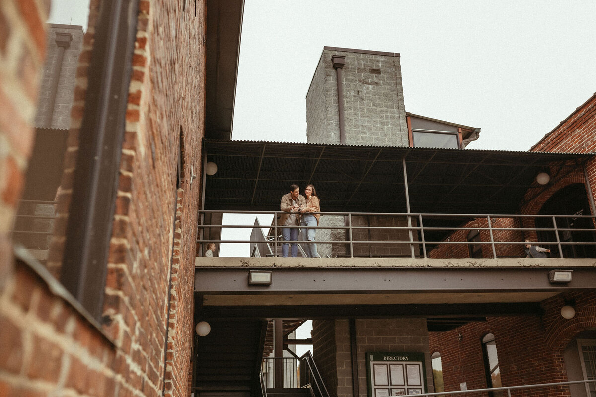 A family of four standing together on a second story walkway looking down at the camera. 