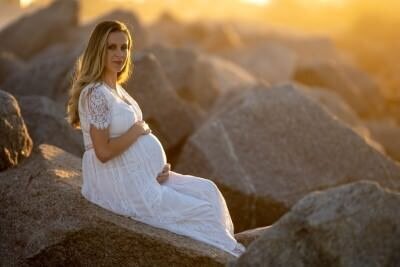 Professional maternity portrait session at golden hour by St Augustine family photographers, featuring expectant mother in white dress on beach rocks