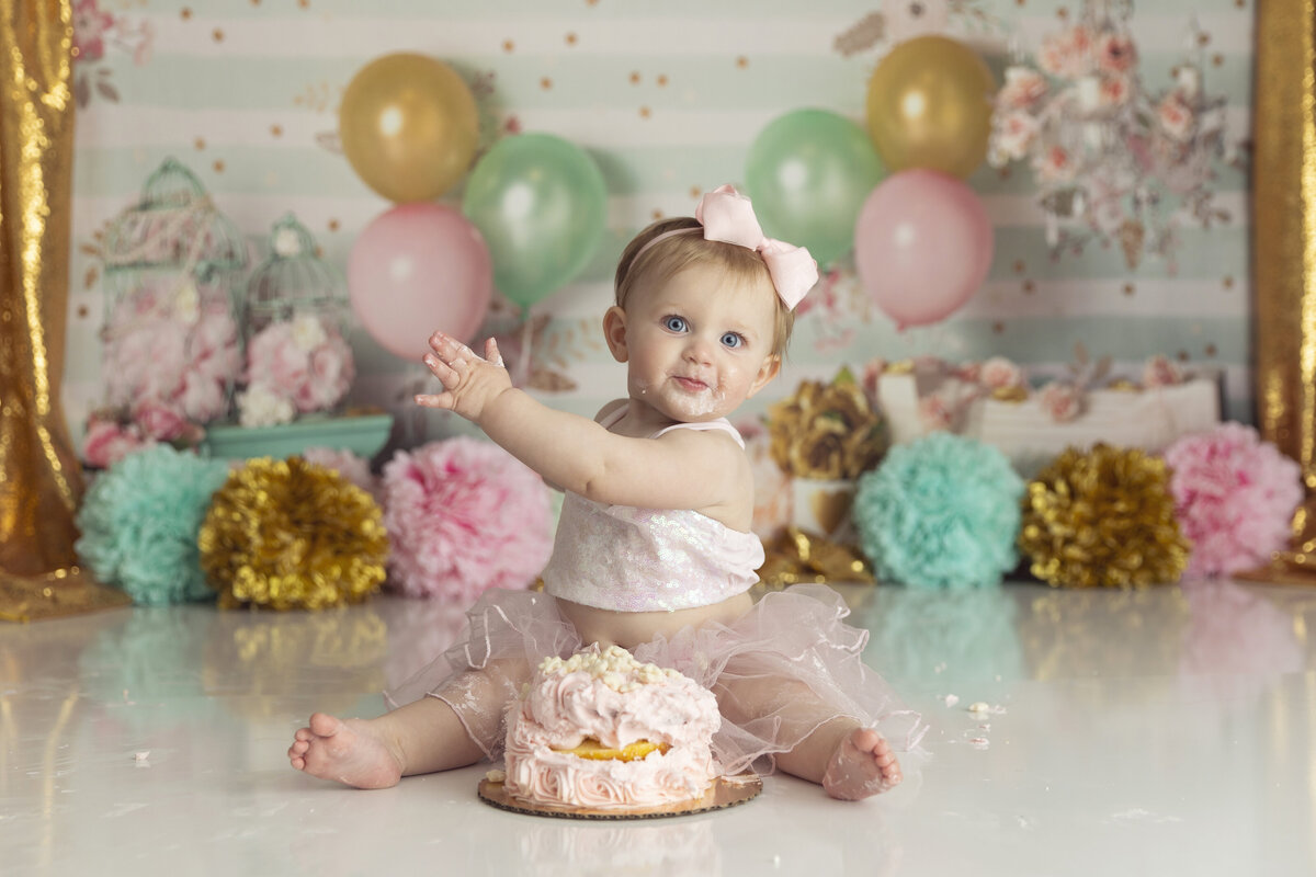 A toddler girl in a pink tutu plays with a cake for a New Jersey Cake Smash Photographer