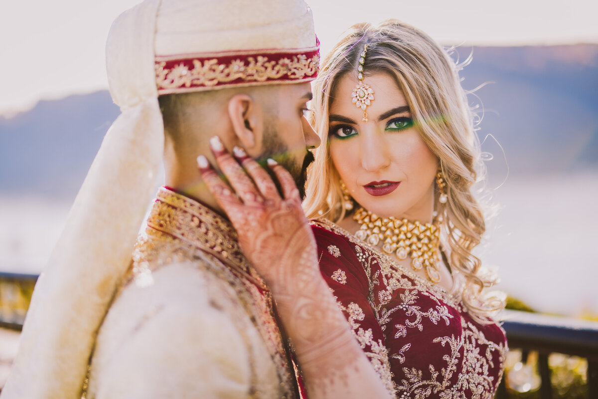 Indian wedding bride holding the groom's face while she looks at the camera at the grandview poughkeepsie