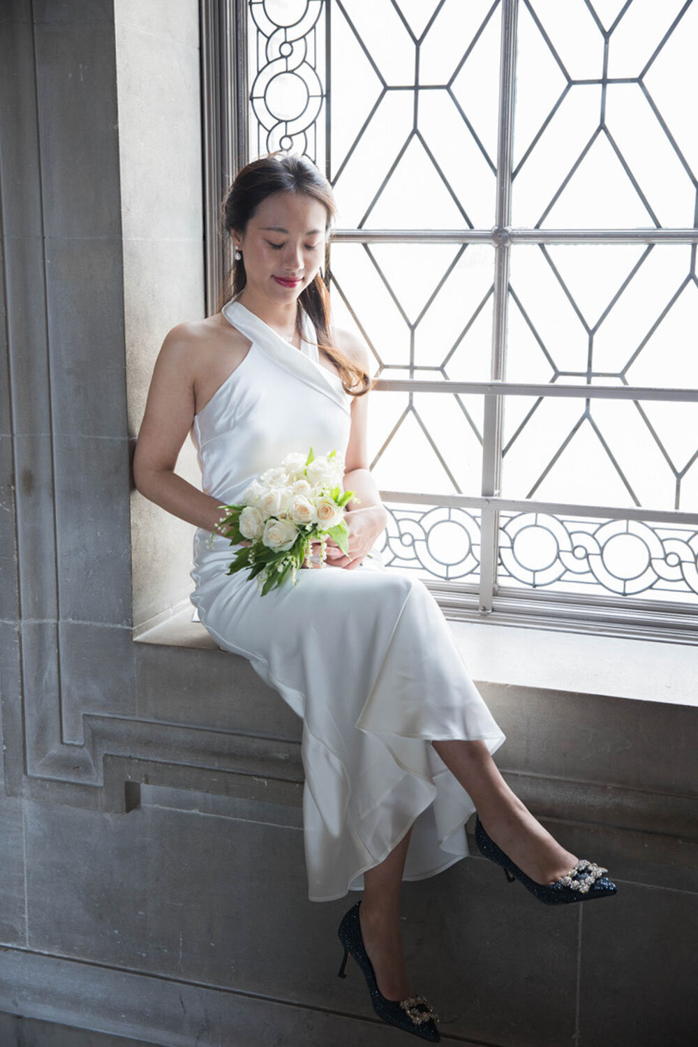 Bride seated on a windowsill with a simple white bouquet