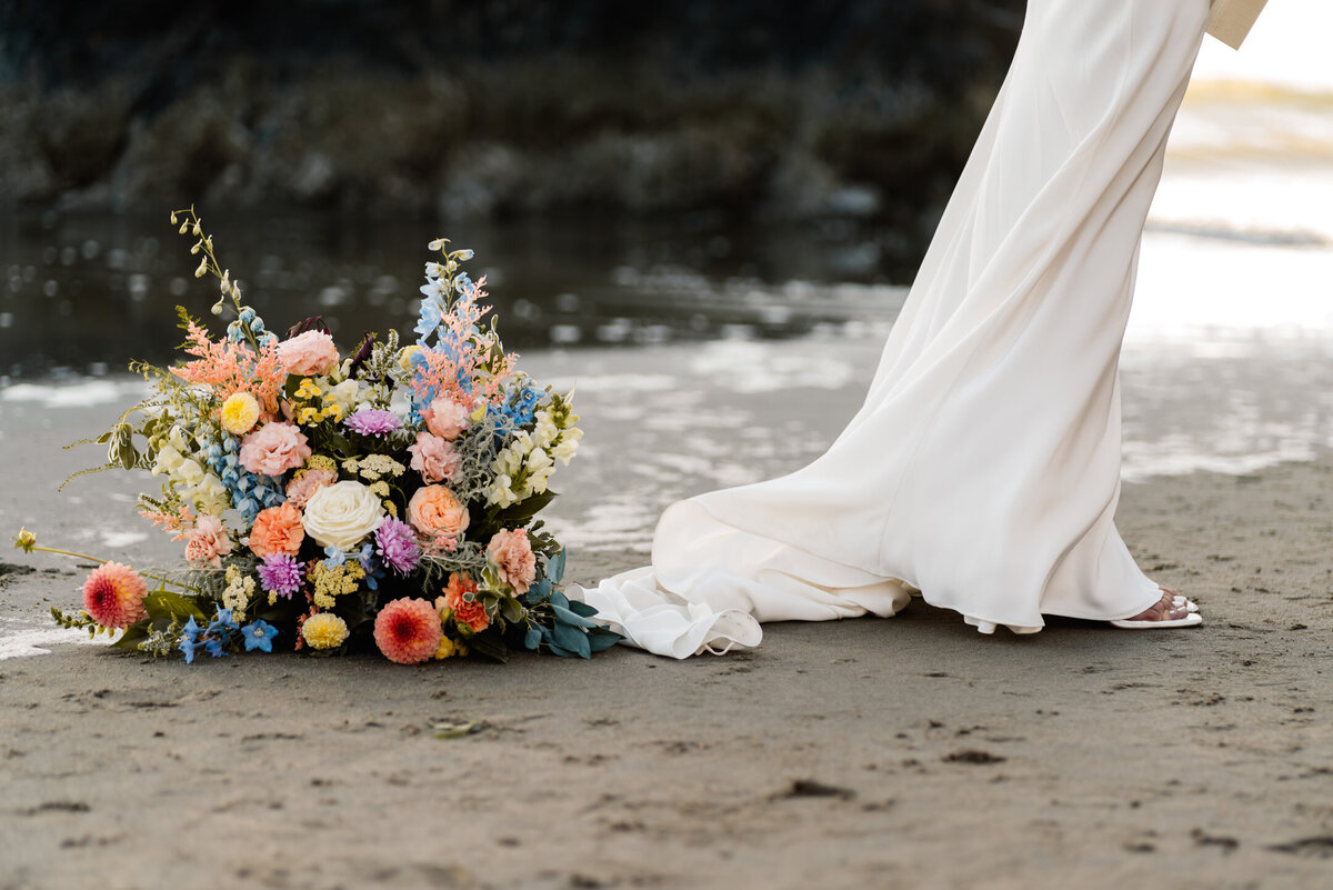 A bride stands next to a bright floral arrangement during her Oregon coast elopement.