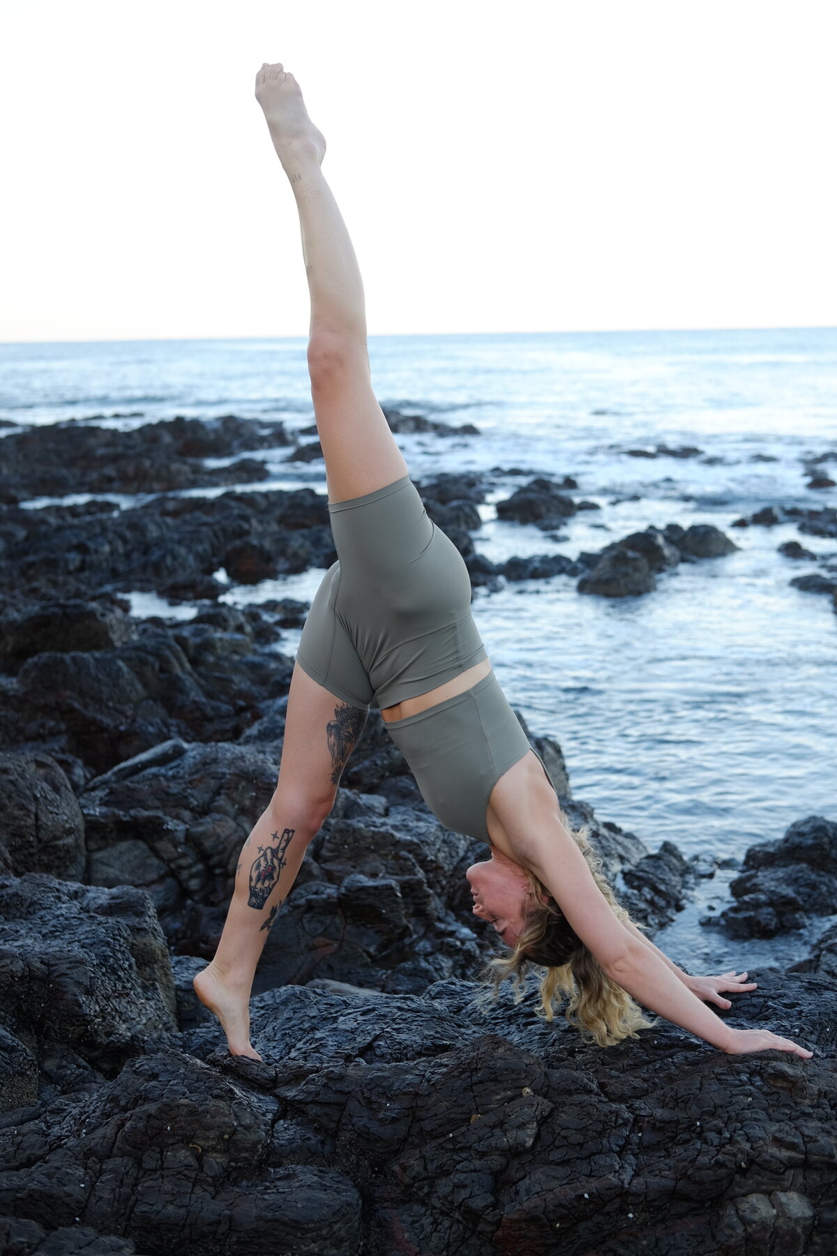 yoga woman on beach rocks in yoga pose with one leg up