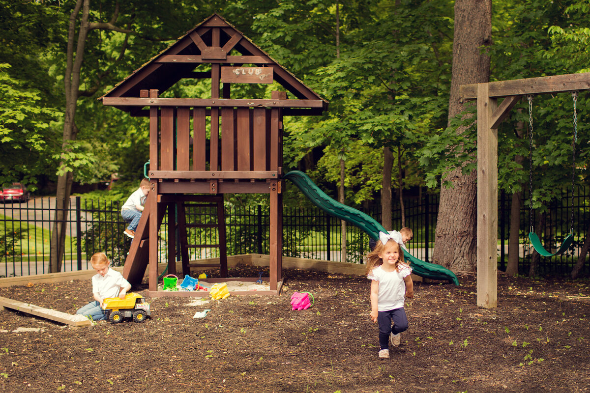 Three kids are playing at a back yard playset after a photo session at their home.