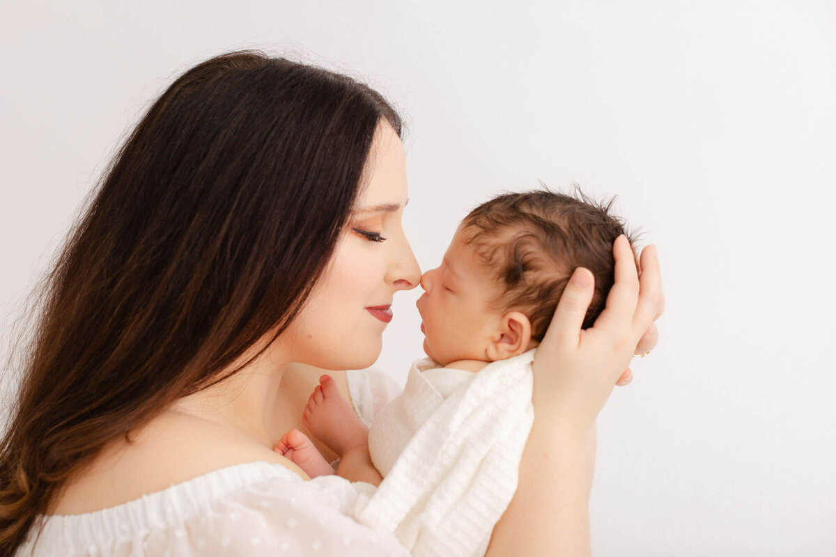 Mom in white dress is holding newborn baby nose to nose during newborn photos in Portland, OR.