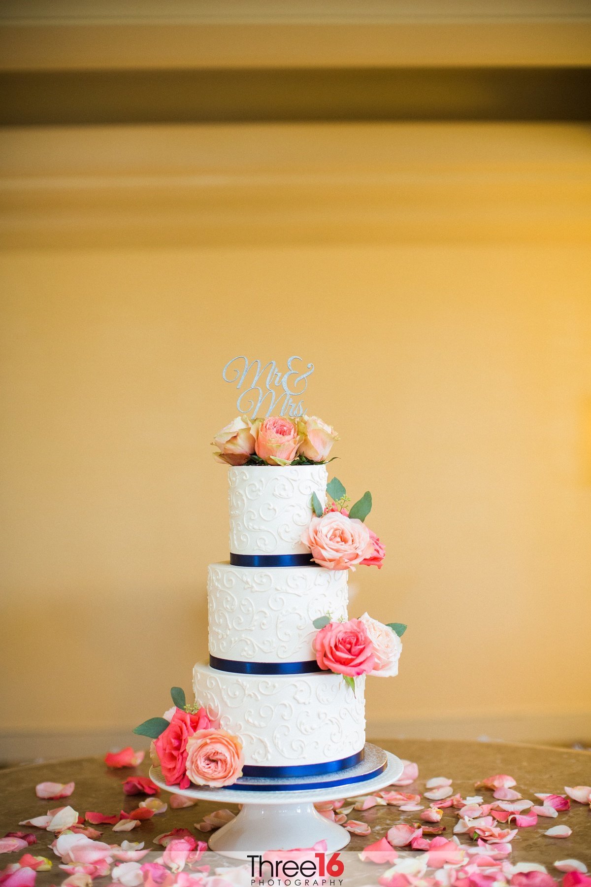 3-tiered white wedding cake surround by rose petals