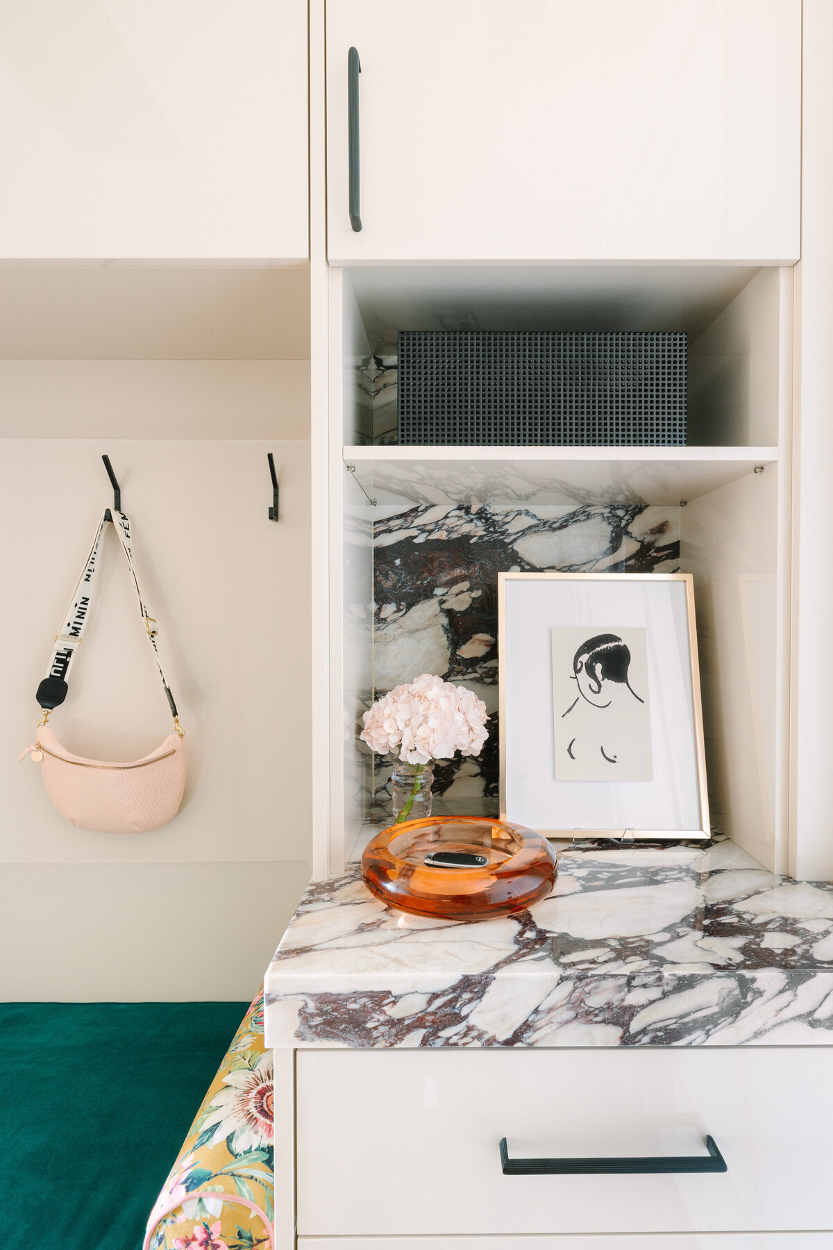 Modern mudroom with beige high gloss cabinets, Calcatta Viola marble counters, and floral cushions.
