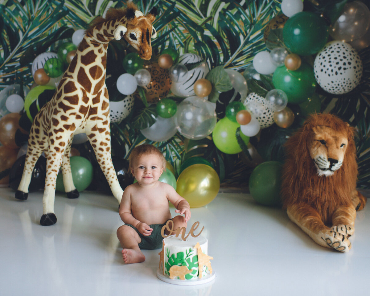baby boy celebrating first birthday with safari themed cake smash