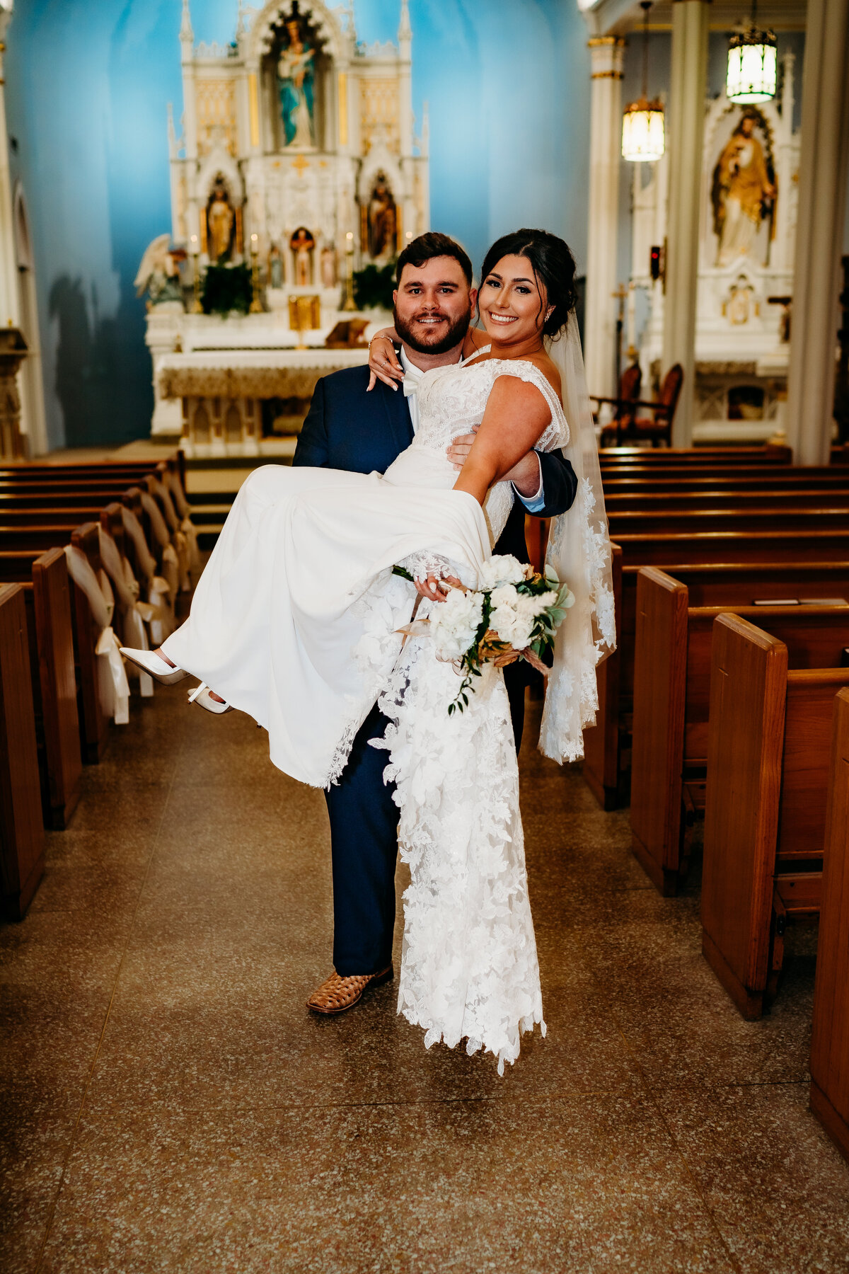 cute pose of groom carrying bride down the aisle in catholic church wedding in Delcambre, la