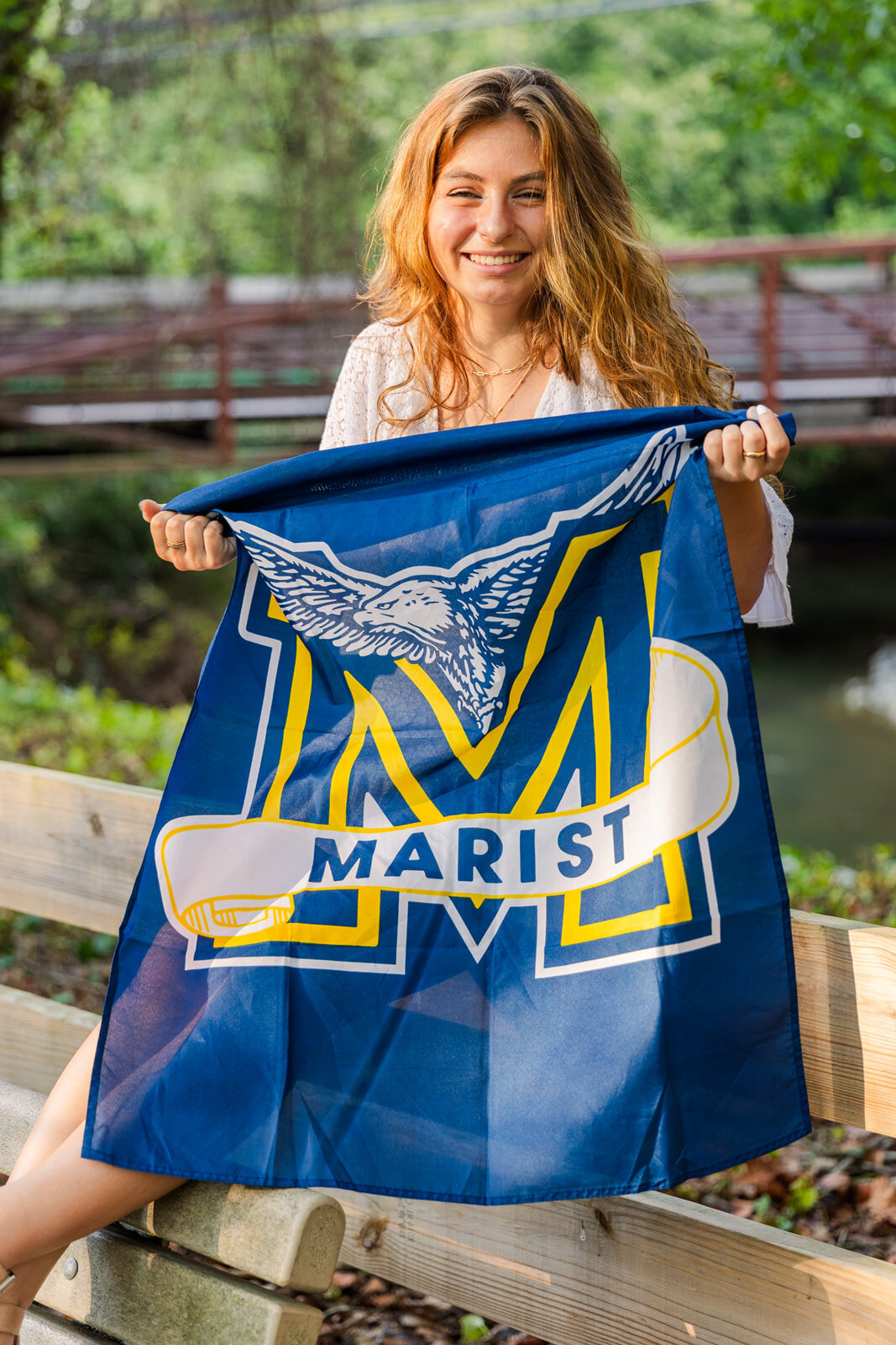 senior girl holding her Marist high shool  banner sitting on a wooden fence