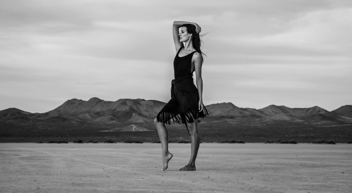 Black and white portrait  Celeste Ziegler standing in desert barefoot one hand resting on her head El Mirage