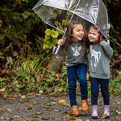 Two little sisters snuggle under an umbrella laughing