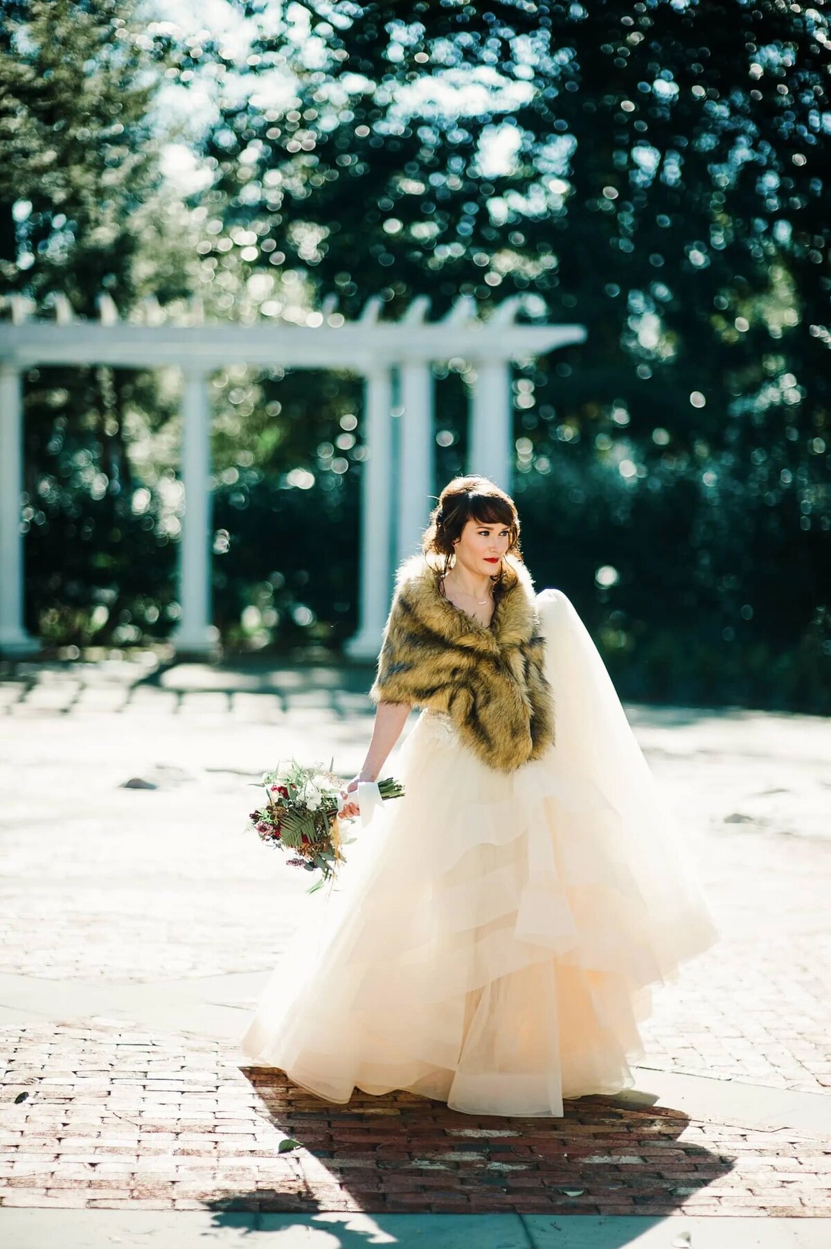 A bride with a fur coat over her shoulders holding a bouquet.