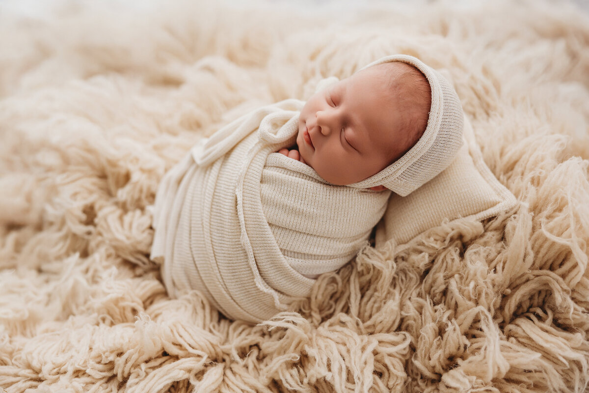 baby posing on tan fur rug for newborn session