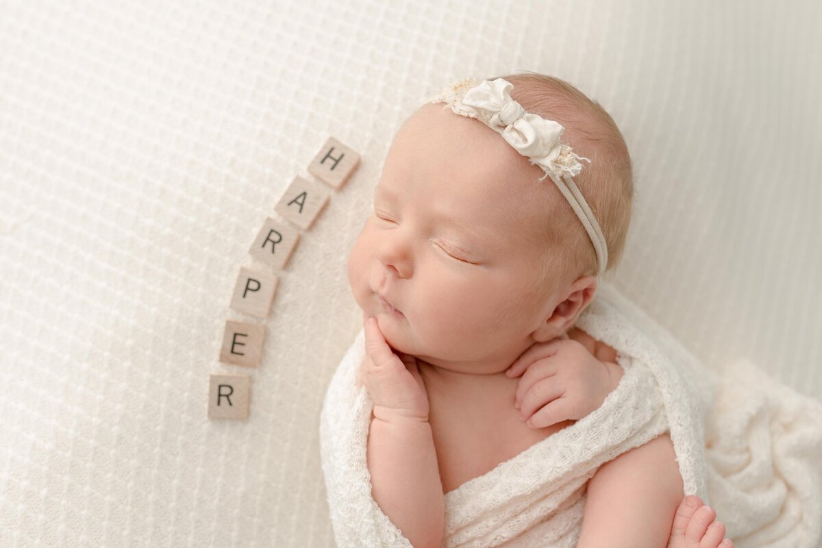 Newborn baby girl swaddled laying down with name spelled out in scrabble pieces
