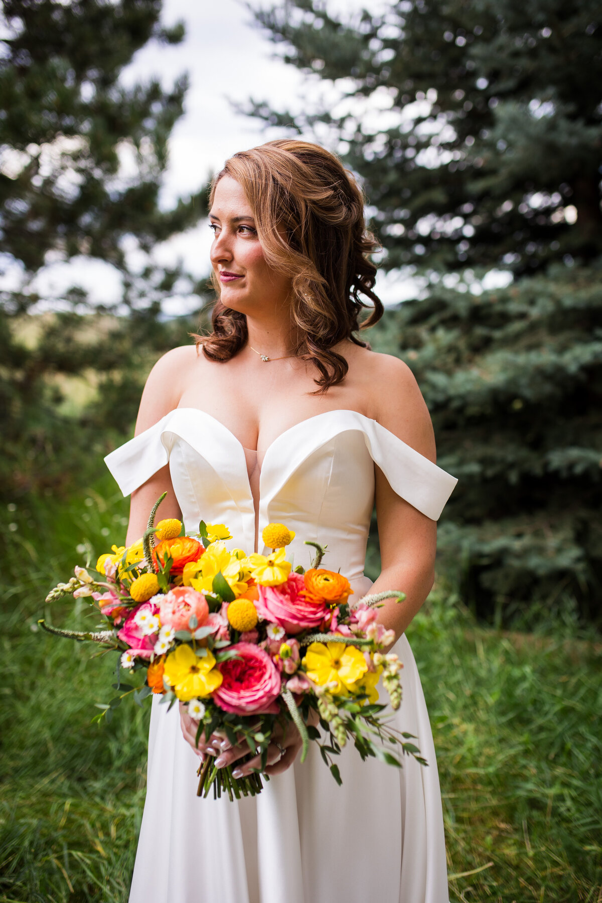 A bride stares off camera with a soft smile on her face, holding her vibrant summertime bouquet.