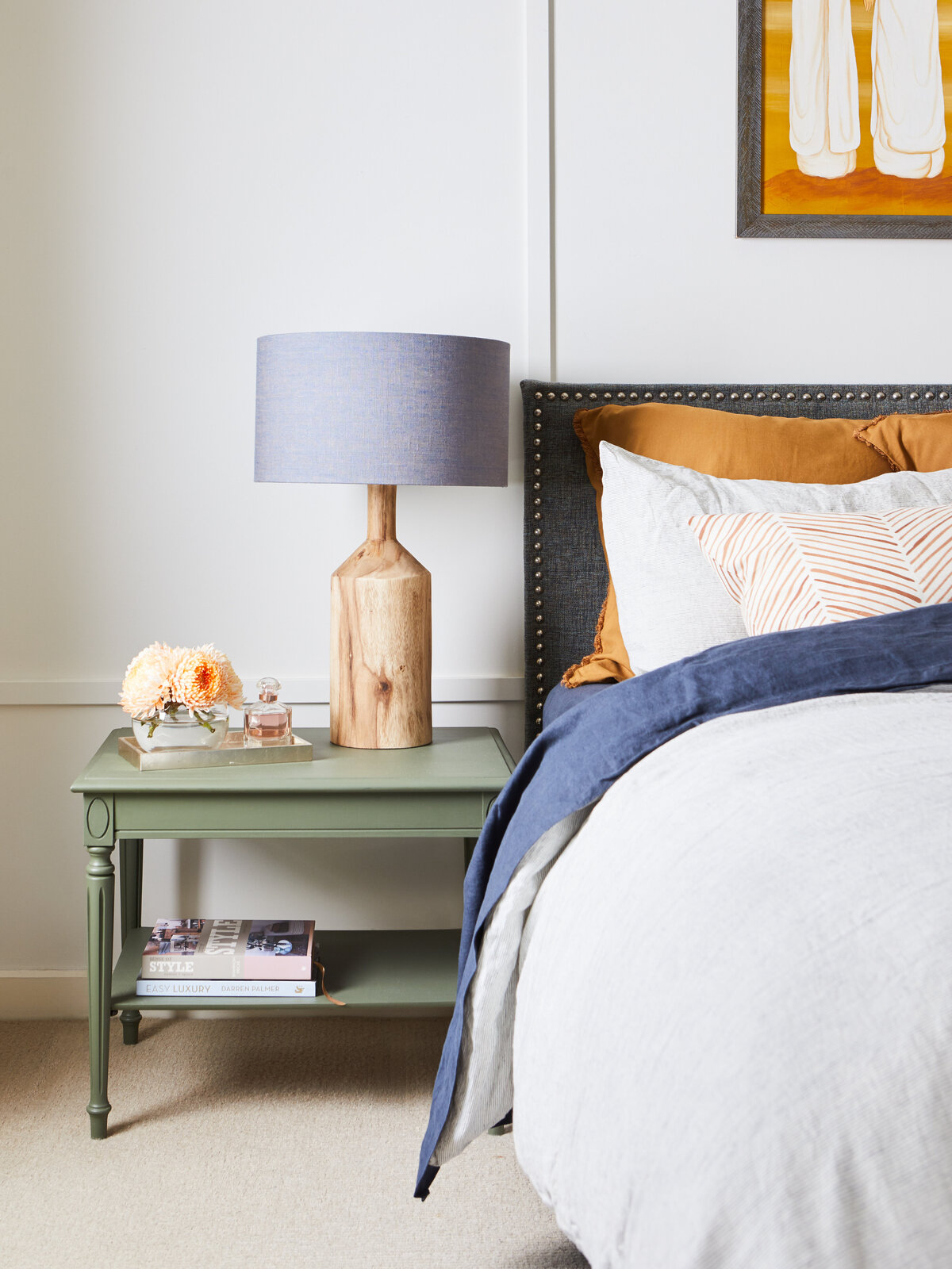 Close-up of styled green bedside table with floral arrangement, perfume tray and wooden lamp in Eynesbury bedroom.