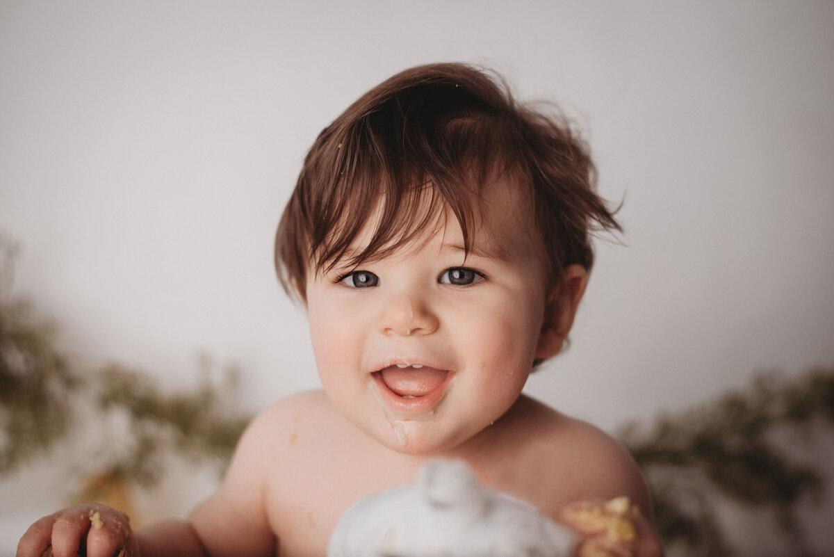 One year old baby boy smiling at camera eating cake