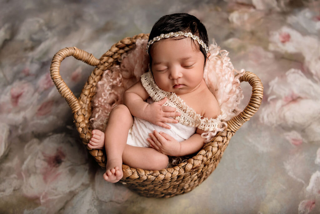 Artistic newborn photography by Connecticut newborn photographer featuring baby in woven basket with lace headband on floral backdrop