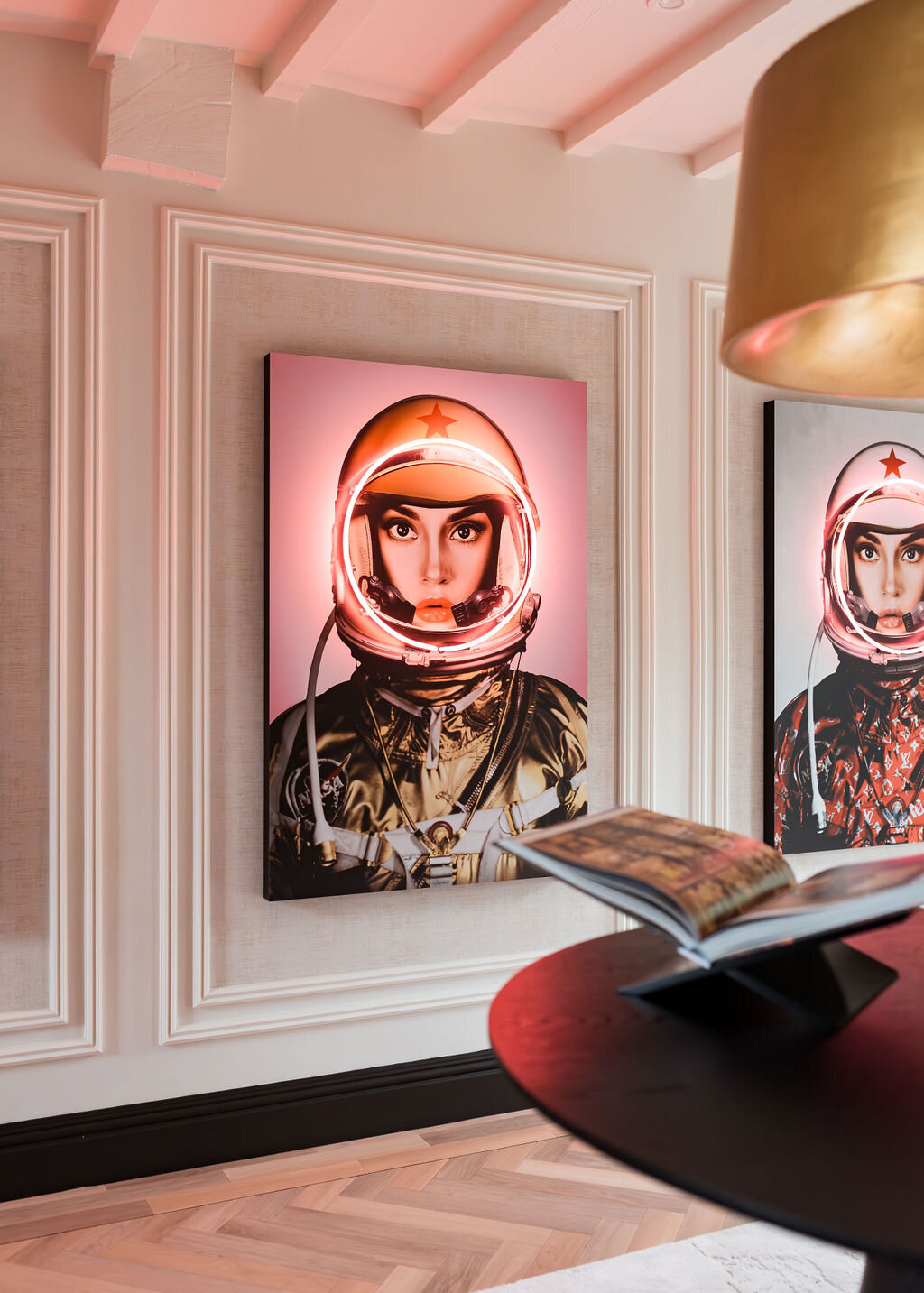 A modern interior features three portraits of astronauts with white helmets illuminated by pink LED, framed on a white paneled wall.