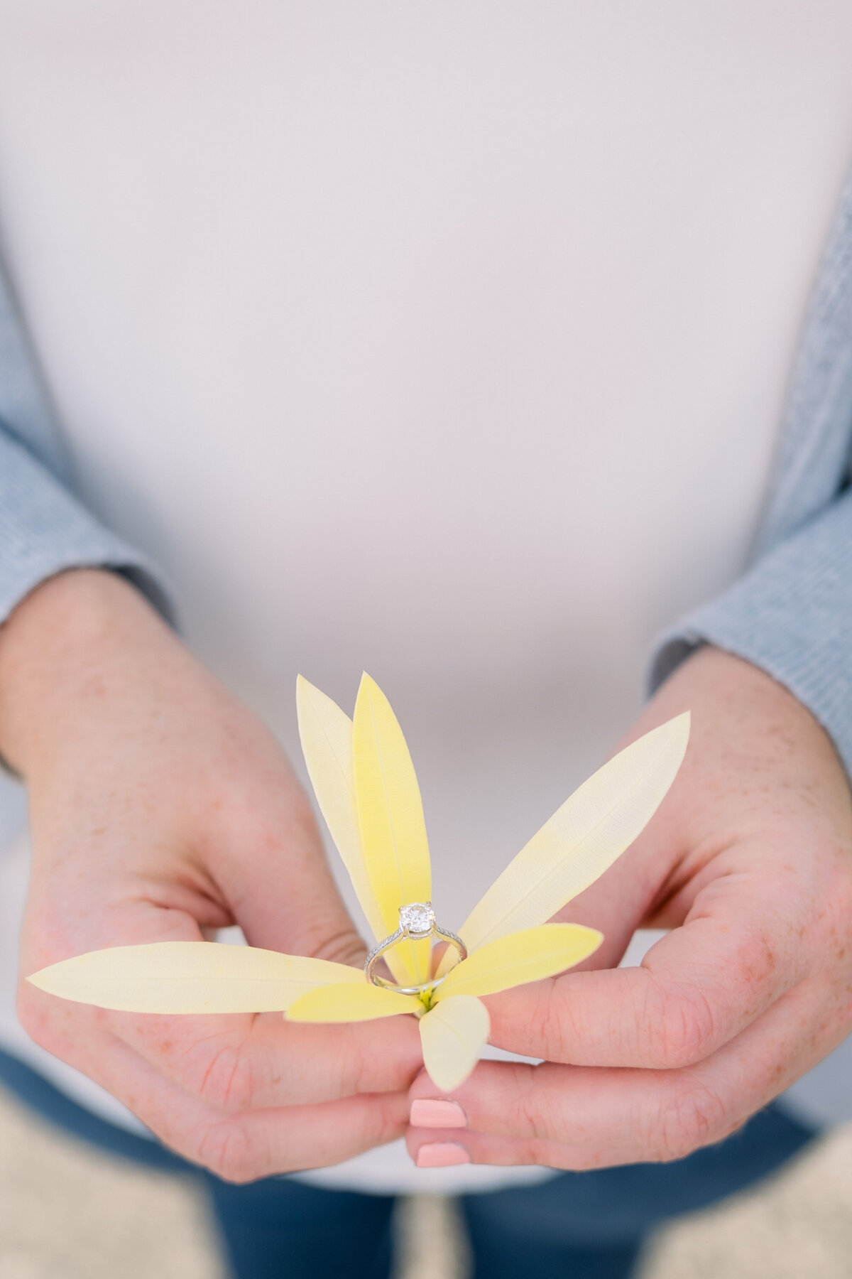 Bride to be holds a colorful yellow flower with her engagement ring inside the flower