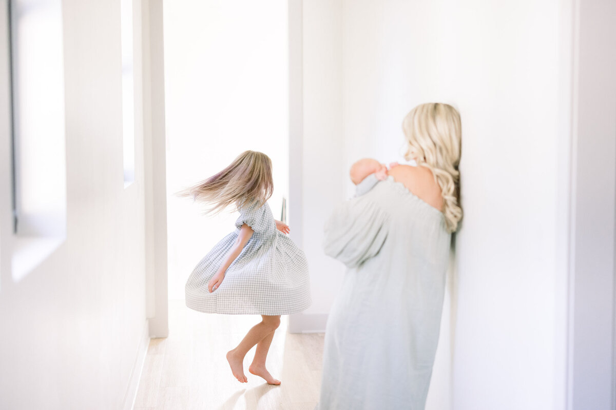 mom holding baby watching sister spin for Tampa newborn photographer Tina Marie Studio.