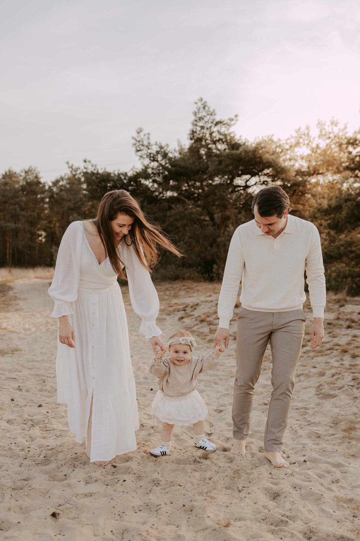 kindje van 1 jaar loopt aan de hand bij papa en mama in het zand 