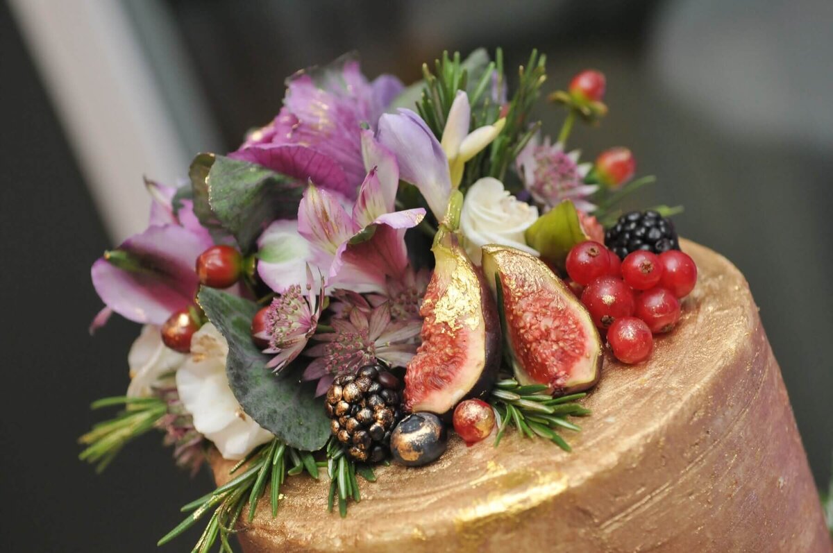 A close of of the top of a gold cake with florals, berries and figs, all with hints of gold
