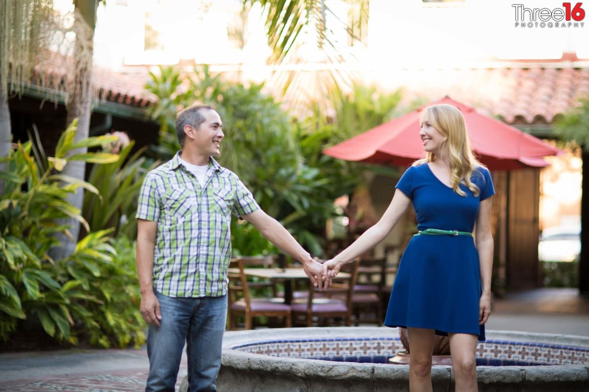 Engaged couple gaze at each other while holding hands in the Villa Del Sol courtyard