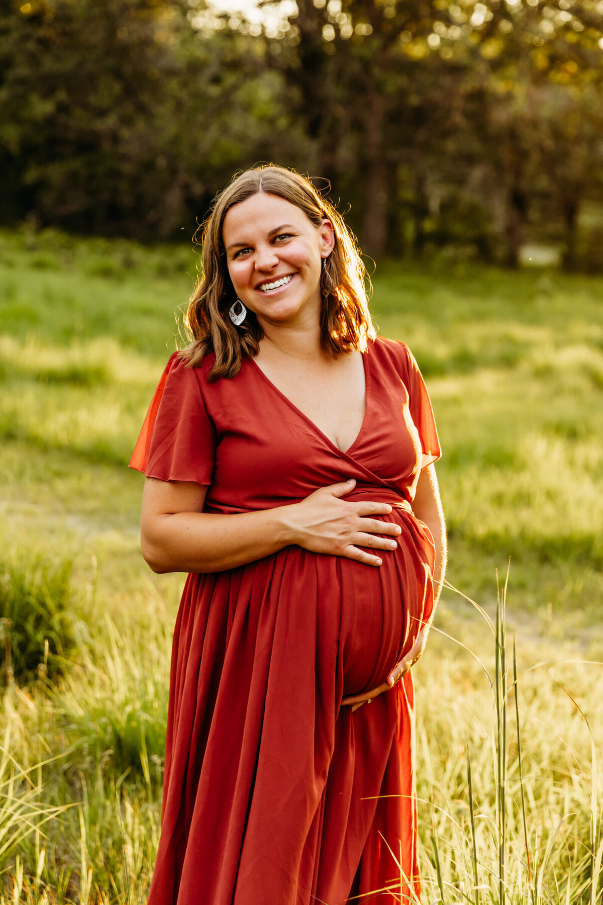 pregnant mom holding bump with both hands in a glowing field near Oshkosh