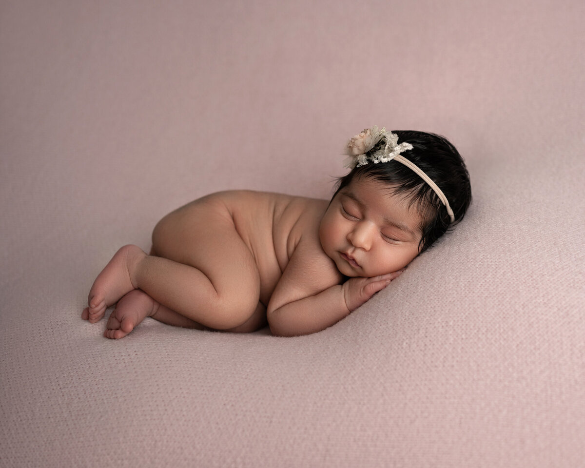 Studio newborn photo of baby girl posed on soft pink backdrop with delicate floral headband | Austin newborn session near Round Rock