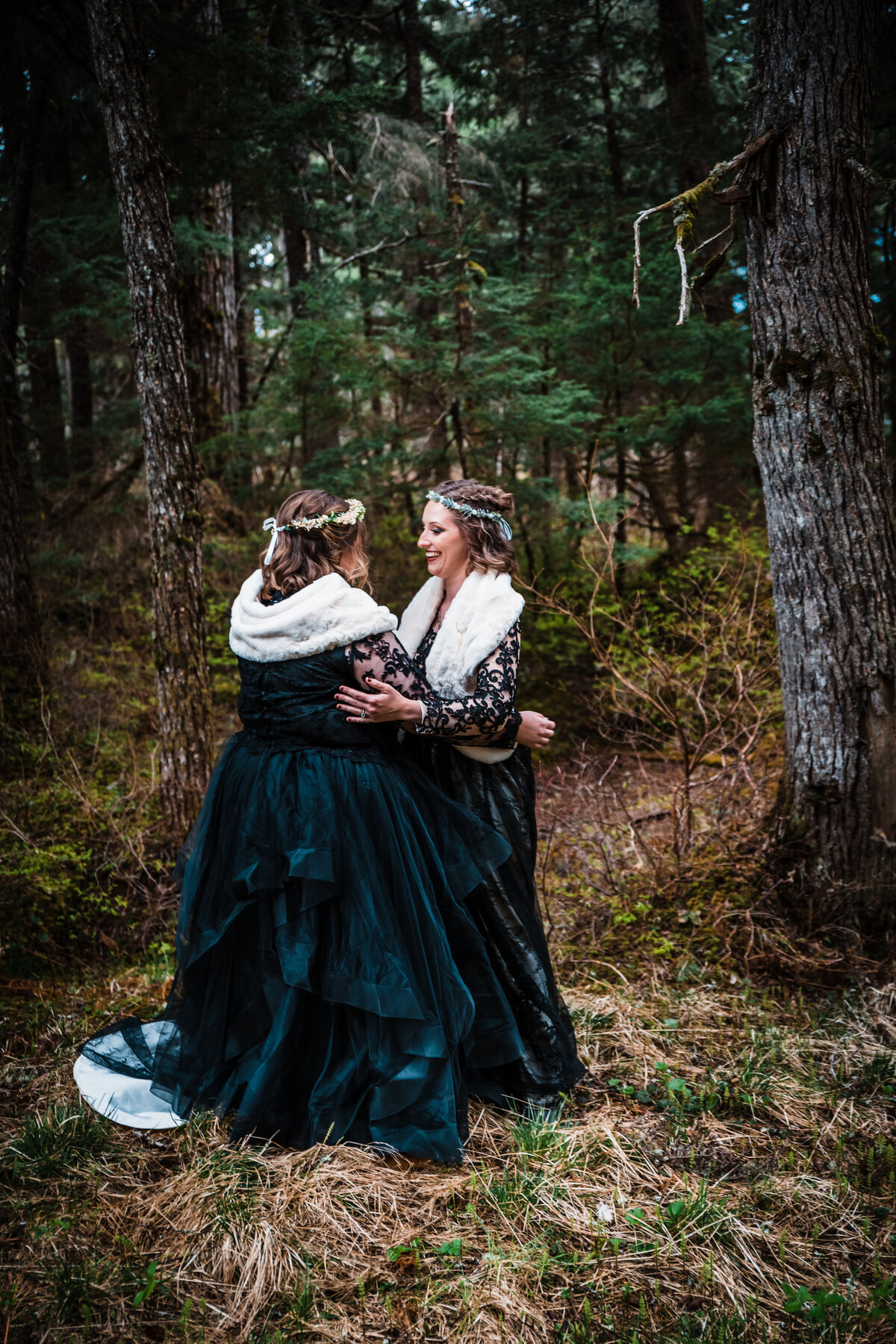Two brides in black wedding gowns embrace during their First Look