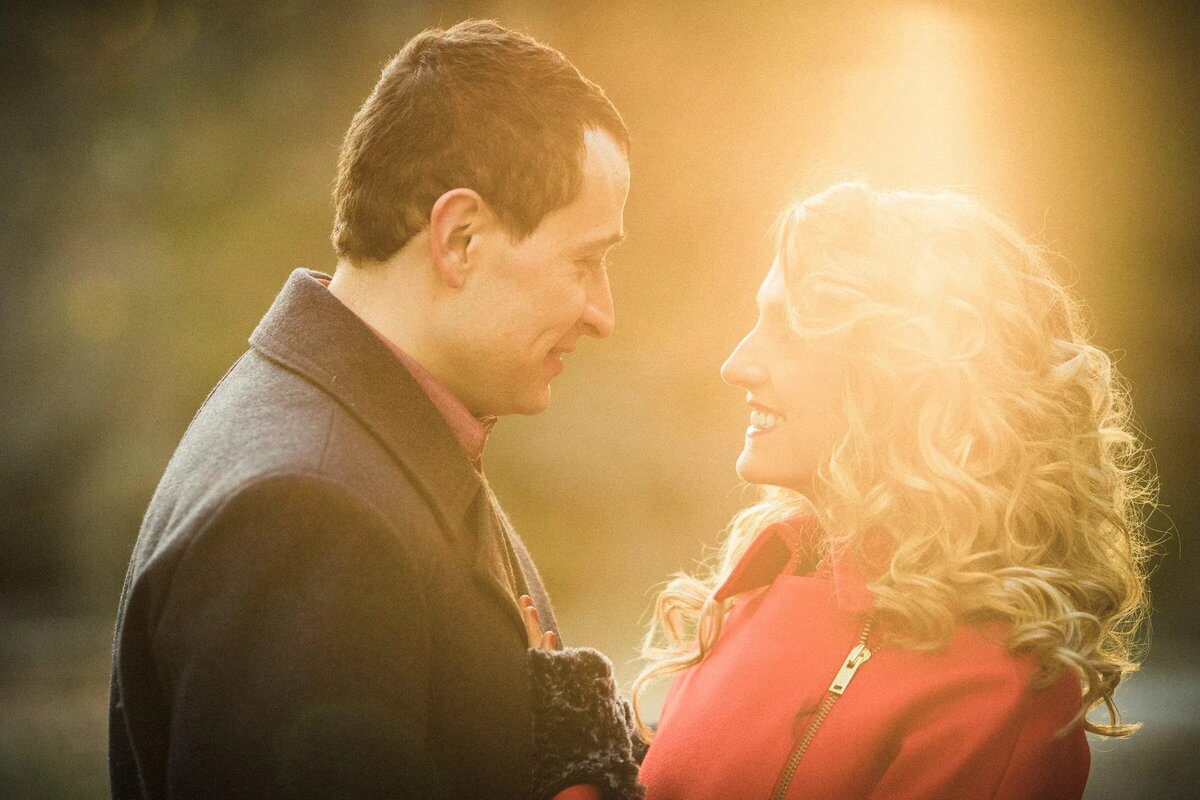 Warm, sunlit photo of a couple gazing affectionately at each other, with a soft focus on the bright autumn leaves in the background