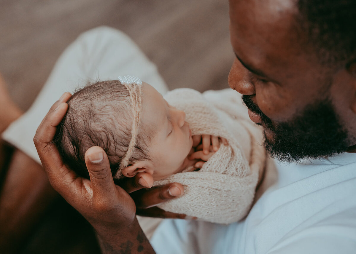 newborn father's hand cradles his newborn daughter's tiny head