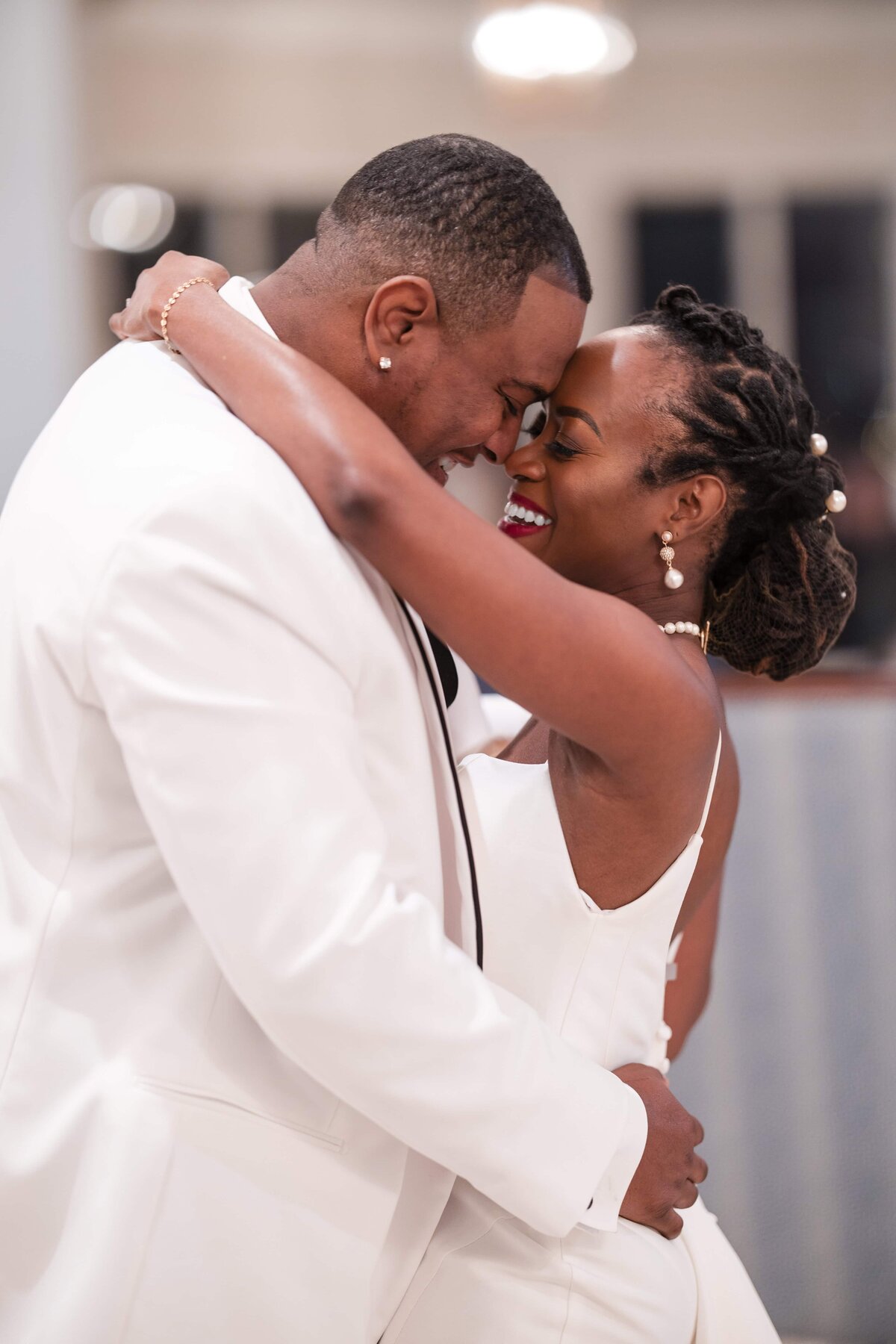 A joyful and emotional moment during the newlyweds’ first dance at Azaleana Manor in Orange Park, Florida. The bride and groom hold each other close, smiling with their foreheads gently touching. The bride’s natural hairstyle, pearl earrings, and elegant gown beautifully complement the groom’s classic white tuxedo. Captured by Phavy Photography in a true-to-color, documentary style that celebrates genuine emotion, connection, and timeless wedding moments.