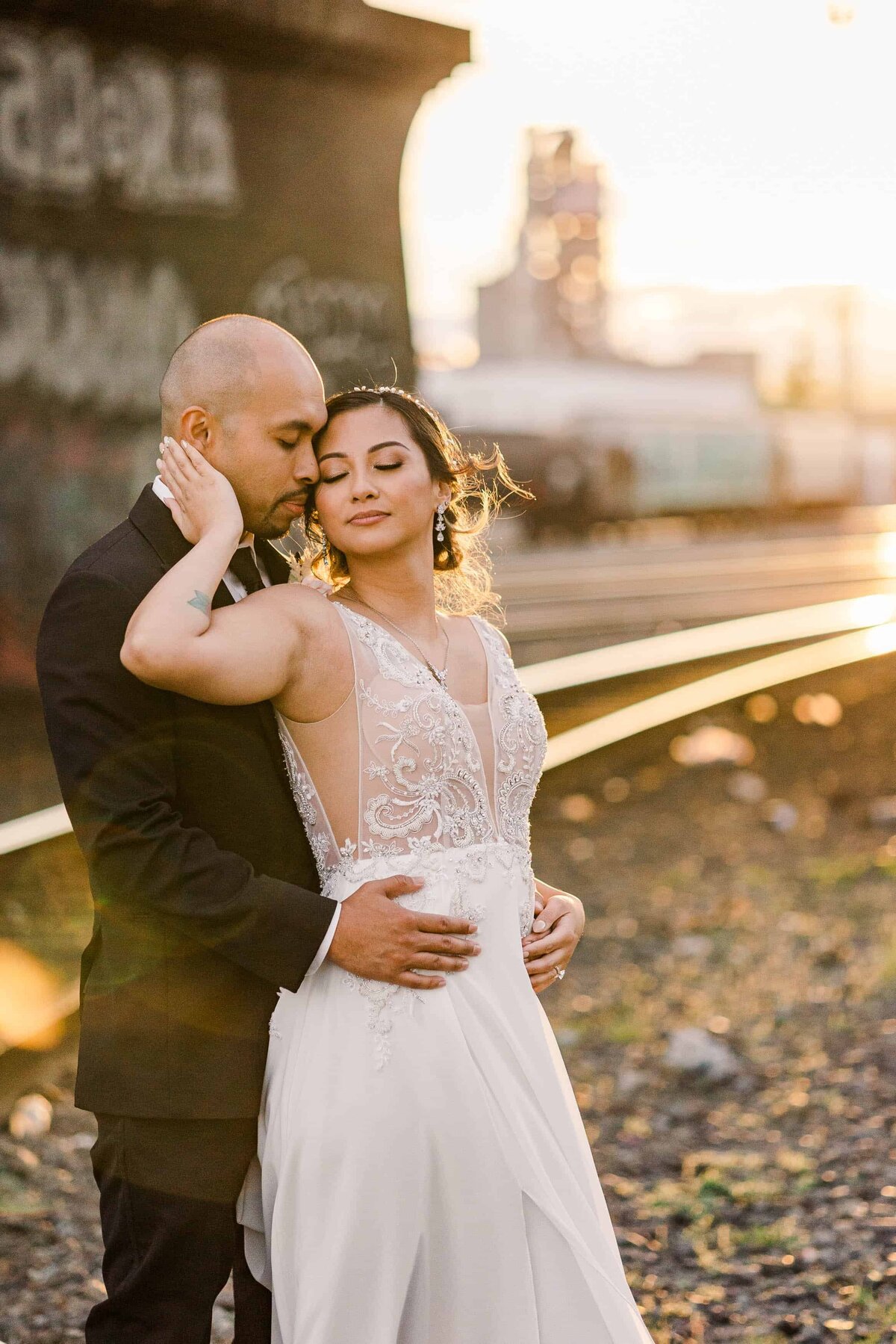Bride and groom snuggled nice and close, with the sunset, falling over the train tracks in the background in South Seattle
