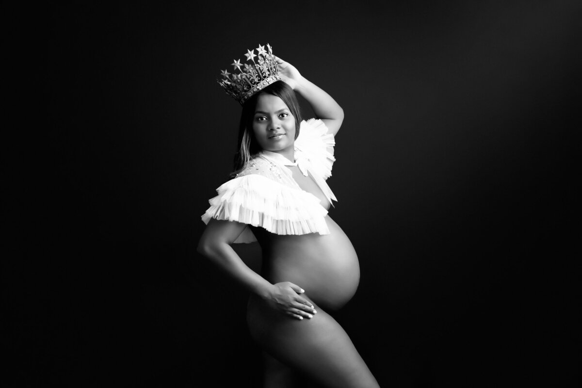 Black and white photo of a pregnant woman wearing a white cape and a crown for her Hamilton Boudoir photographer session
