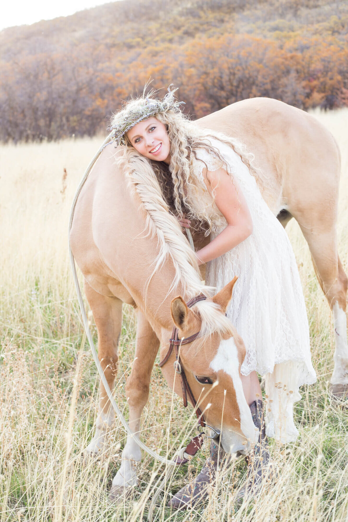 Blonde young woman leaning on a palomino horse in a field of dry grass