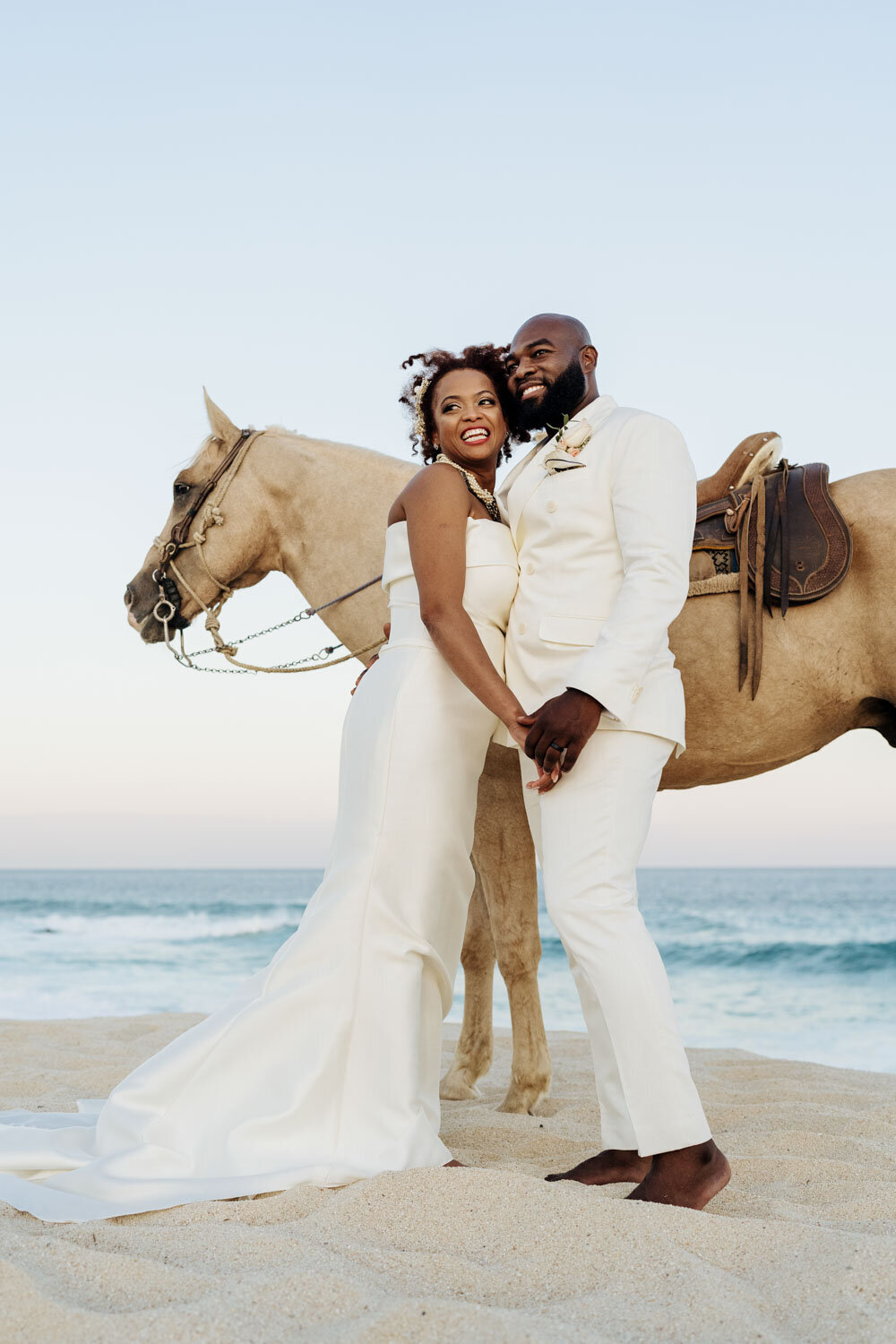 Bride and groom posing with a horse on a beach at sunset