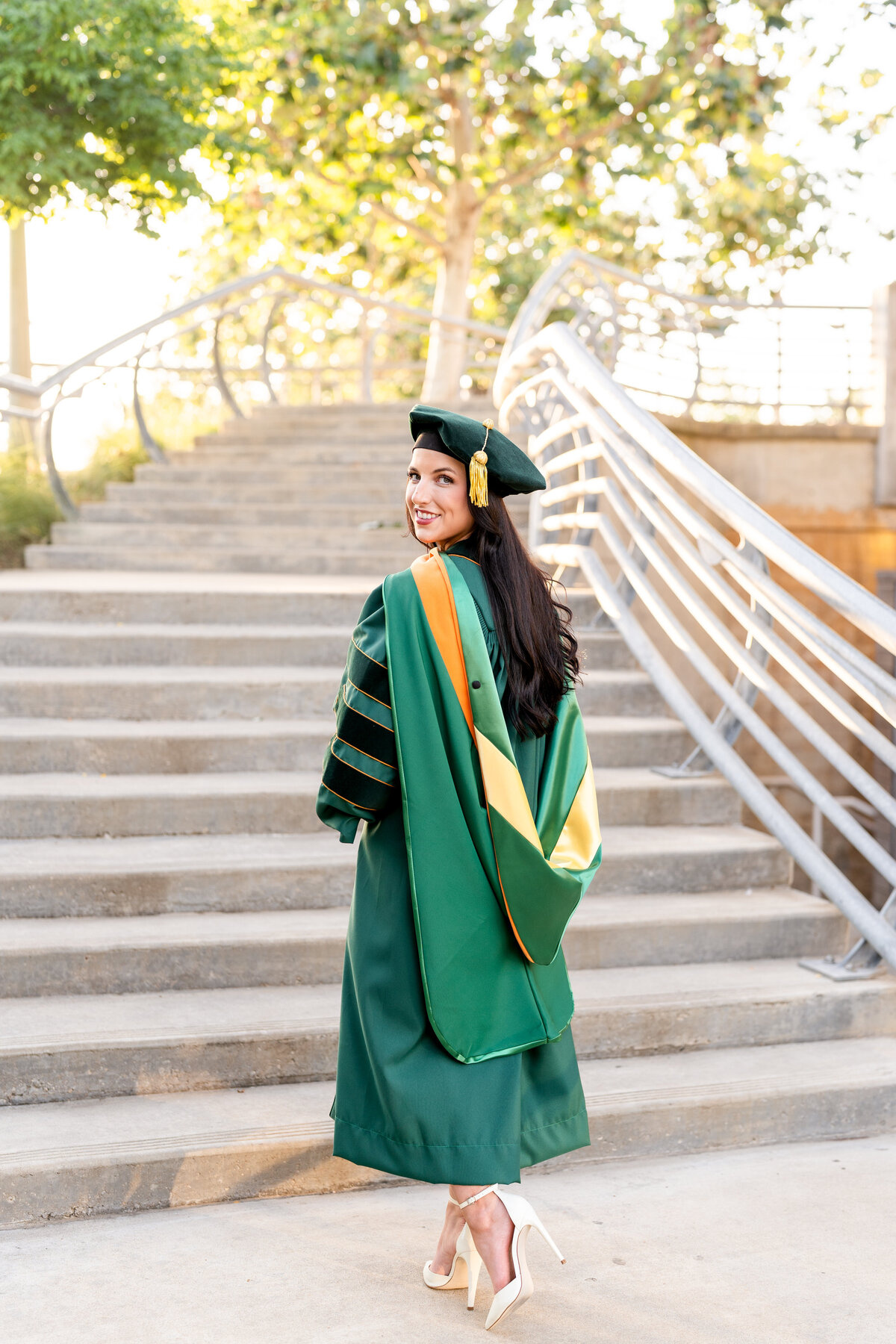 Baylor senior girl dressed in doctorate gown, hood and hat and looking back over shoulder while standing in front of stairs in Downtown Houston