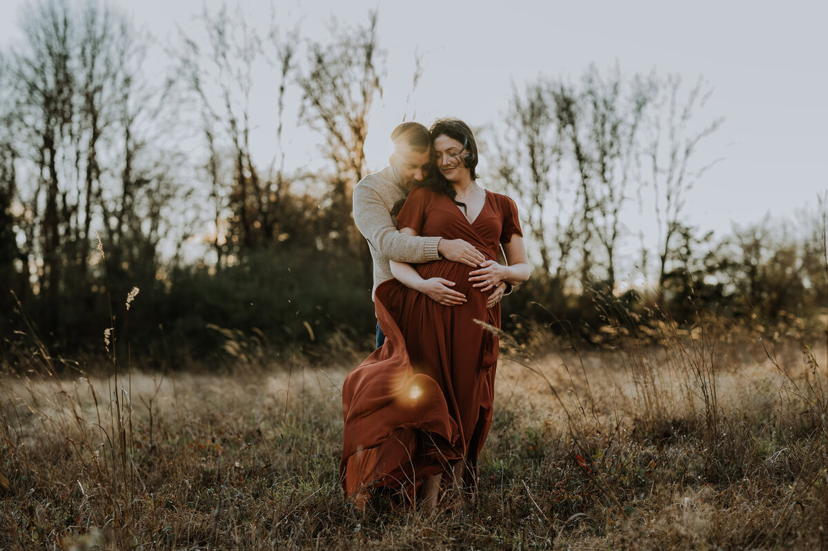 man hugging pregnant wife at golden hour while the wind blows