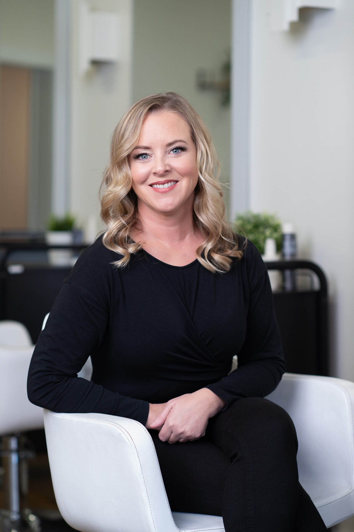 a hair salon owner dressed in black sitting in her white salon chair smiling at the camera.  Captured on-site at Richardson Hair Design by Ottawa branding photographer JEMMAN Photography