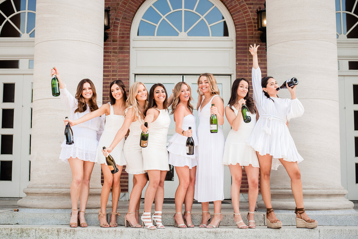 College senior girls standing on stairs toasting to graduation with champagne bottles