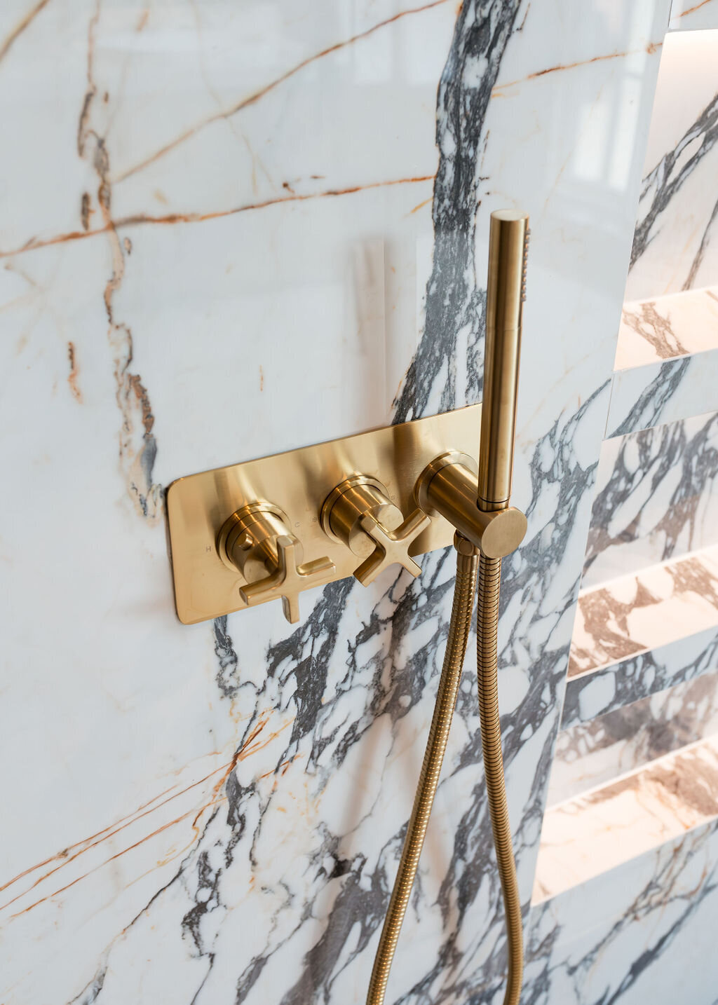 Modern gold shower fixtures mounted on a white marble wall with black veining.