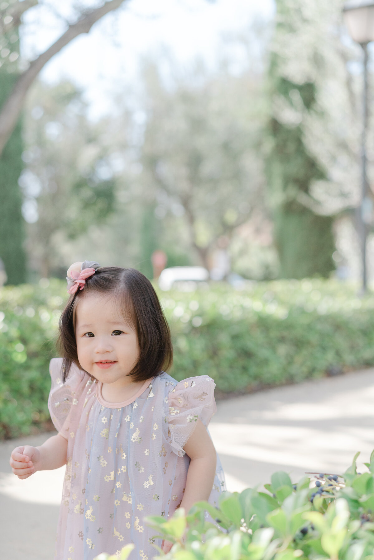 little girl with bow and pink dress walking in park