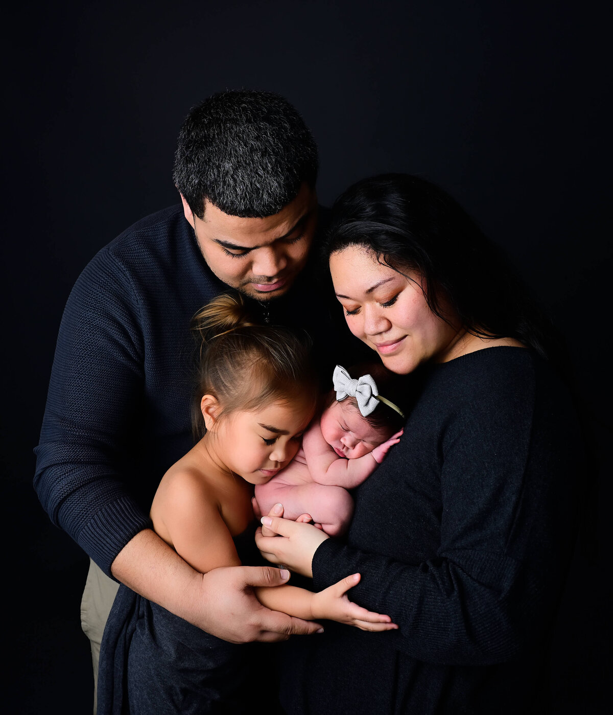 Low key lighting for a newborn photoshoot with family including baby, older sibling, and parents. Image by Kitsap Peninsula photographer Beth Benecki of E. Benecki Photography.