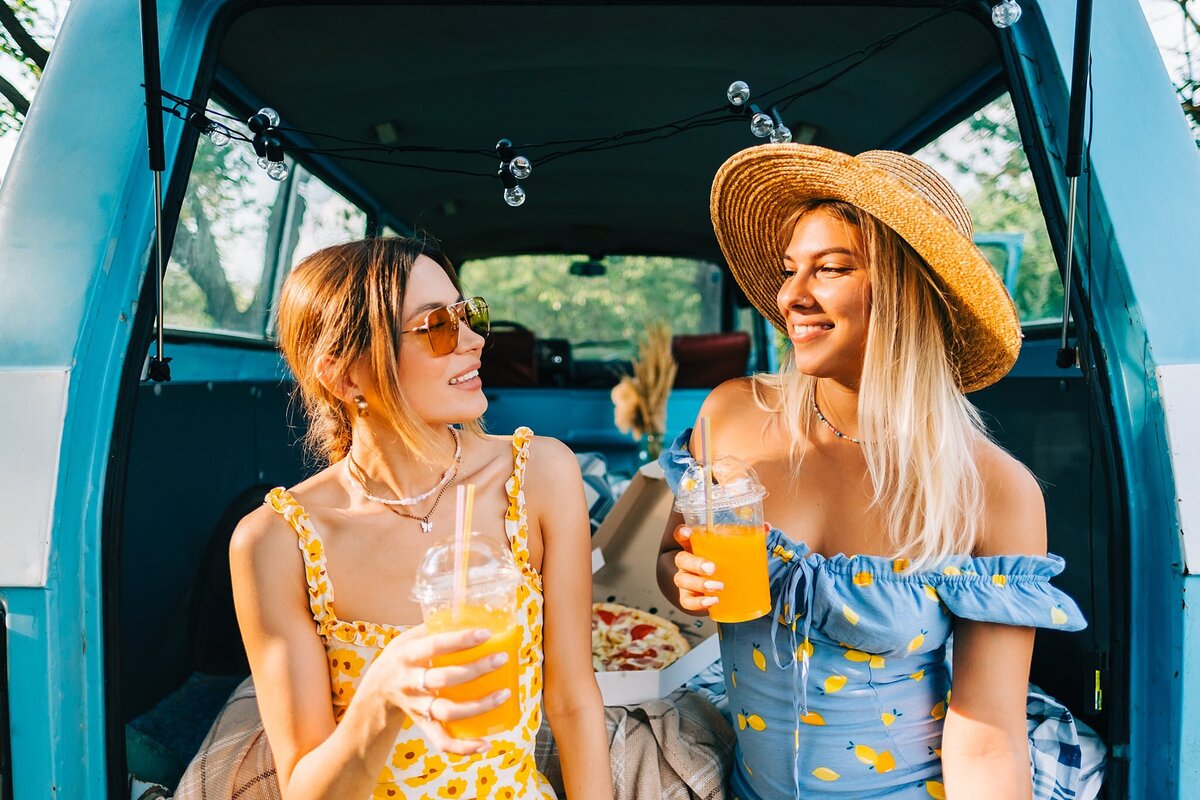 Girls smiling at each other while drinking juice in the back of a trunk