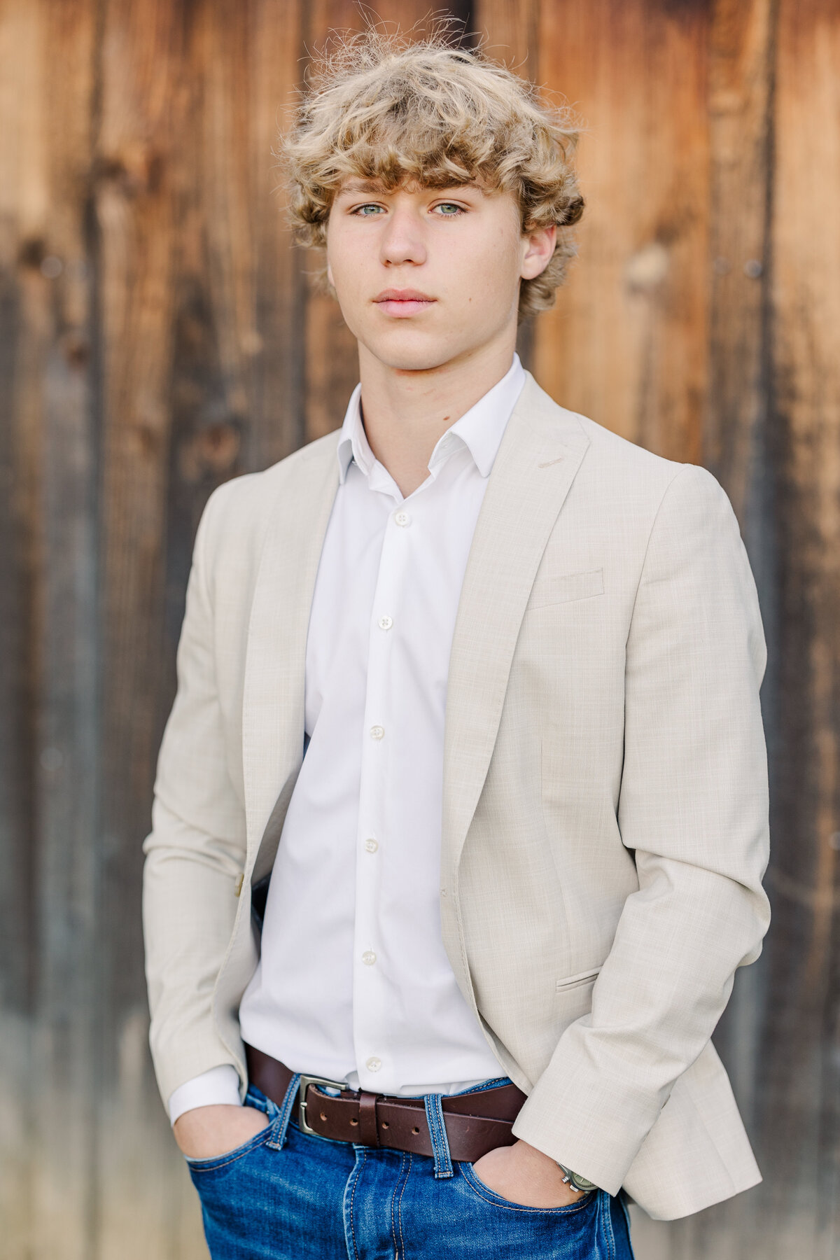 senior-guy-staning-next-to-barn-wearing-jeans-and-a-nuetral-blazer