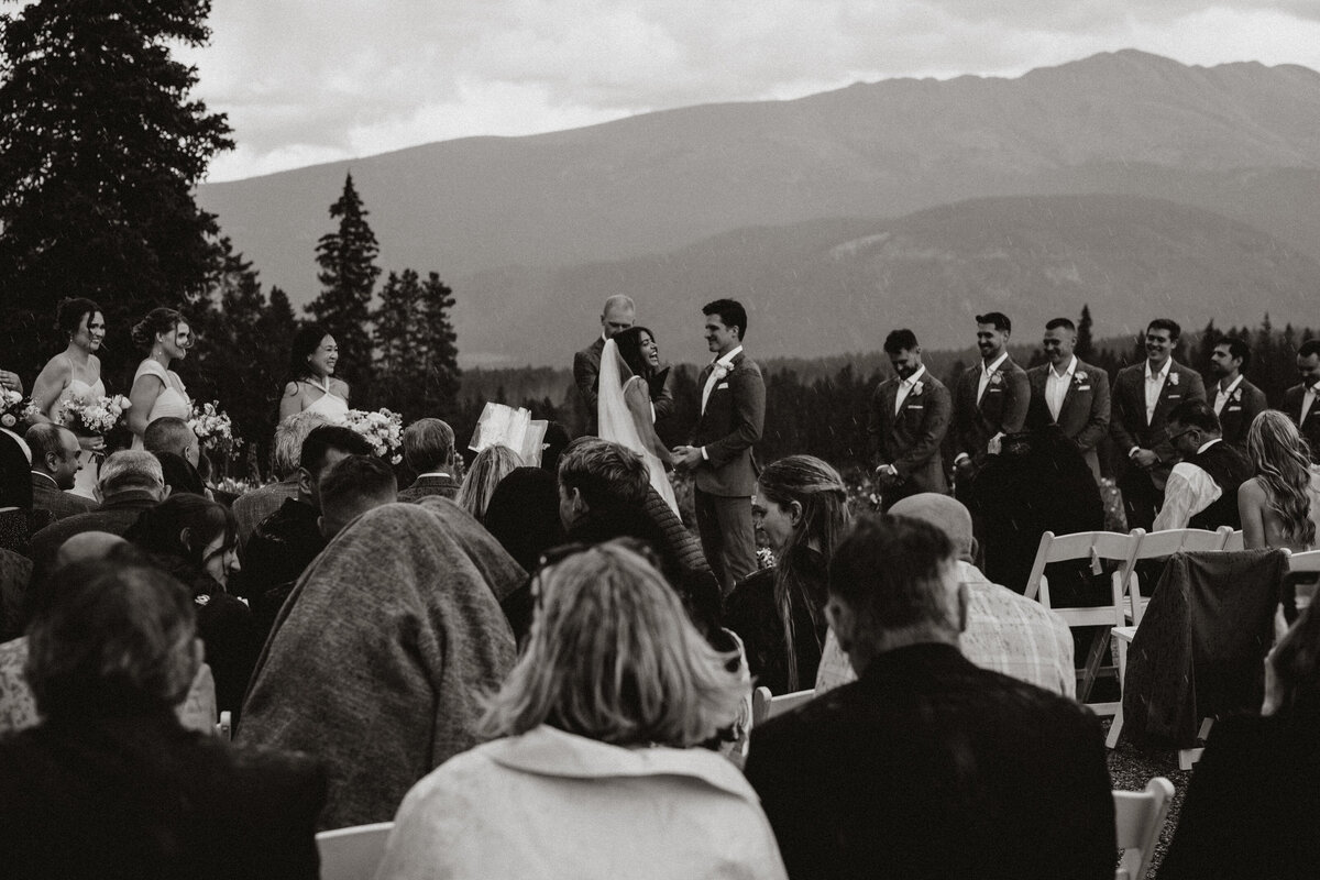 Black and white shot of mountain ceremony with couple exchanging vows and wedding party in view.